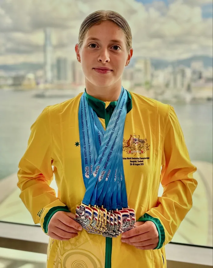 An Australian team swimmer in the green and gold, holding a fan of medals from the 2025 Virtus World Swimming Championships in Bangkok